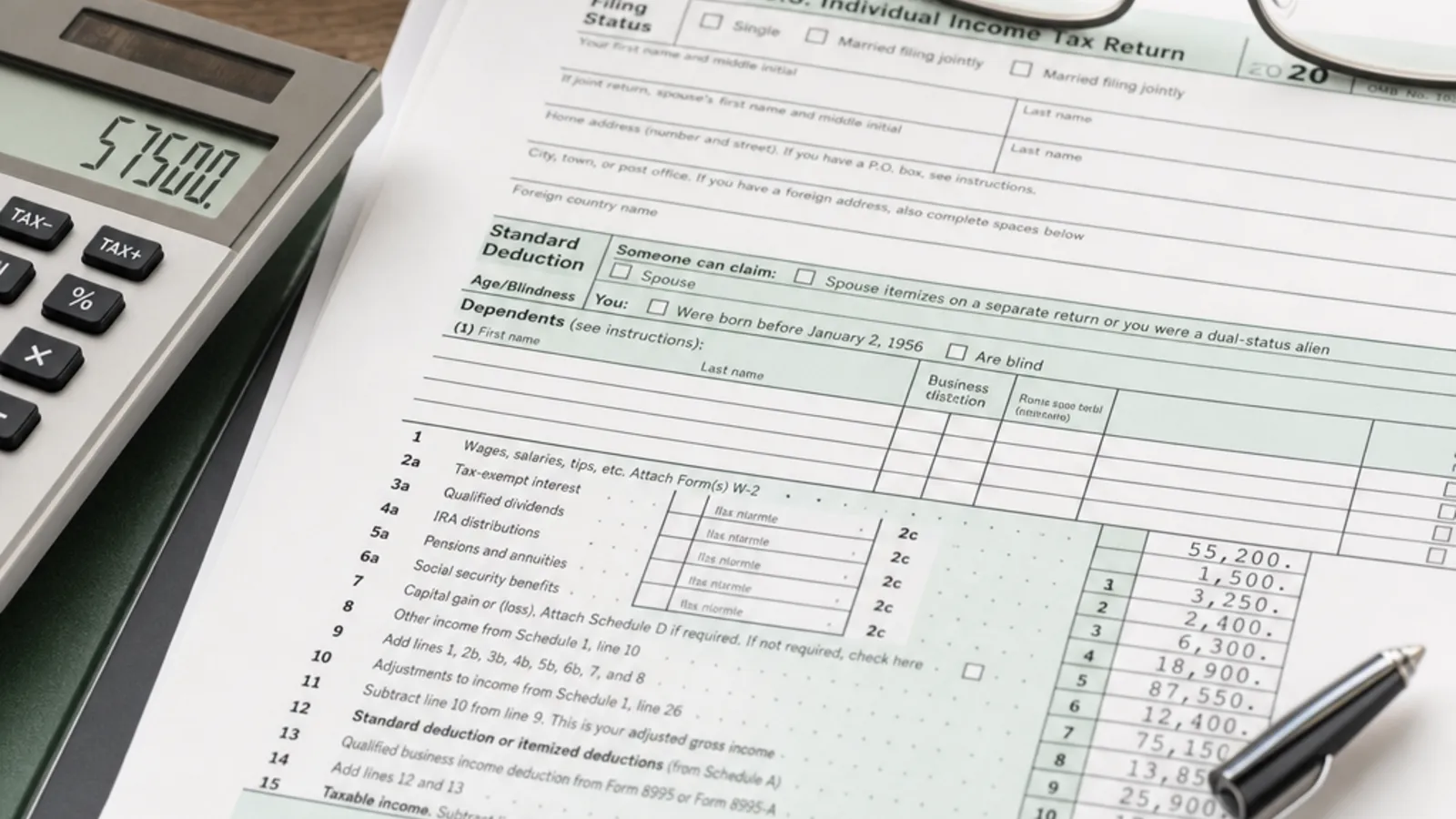 A US federal income tax return form beside a calculator, reading glasses, and a pen